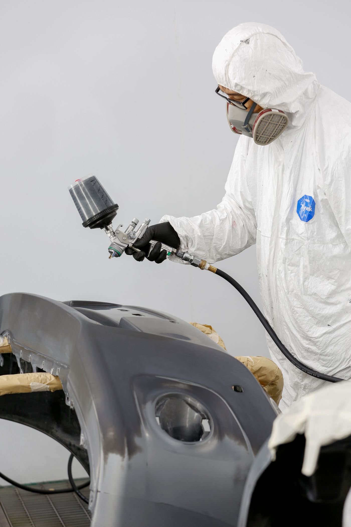 Painter in a spray booth refinishing a bumper cover with an HVLP spray gun