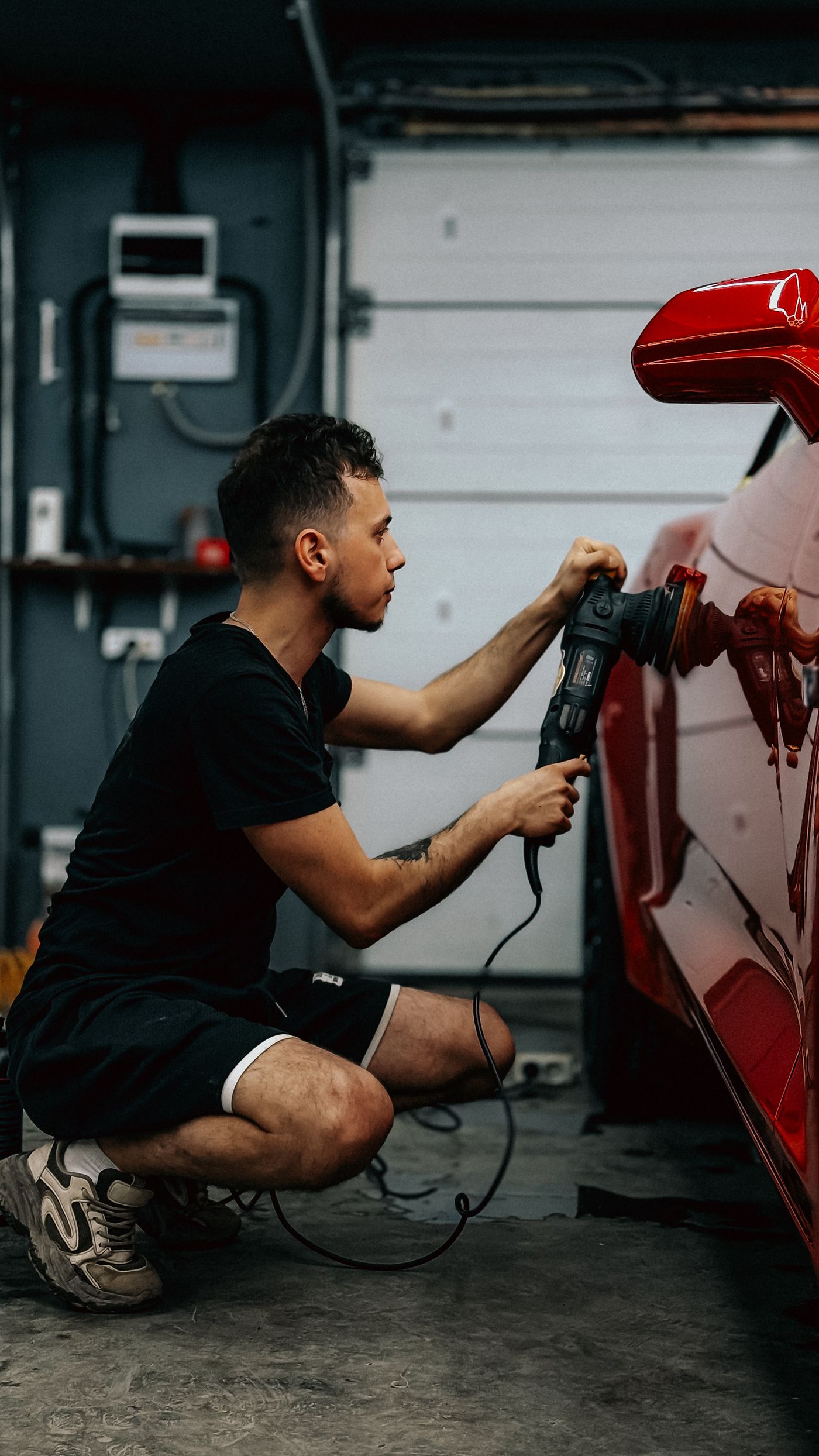 Technician machine-polishing scratched paint on a red car panel